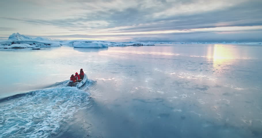 Antarctica travel and exploration, people riding motor boat. Zodiac boat sailing cold polar ocean water surface in sunset light. Discover the beauty of South Pole. Aerial winter landscape, drone pov