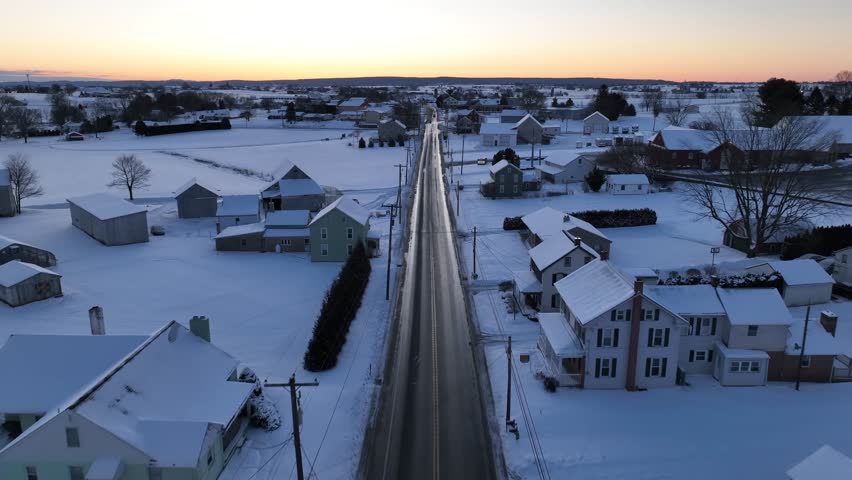 American countryside during winter sunrise with snow covered landscape. Aerial over rural country road.