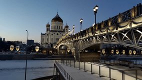 Side view of Cathedral of Christ the Saviour next to illuminated bridge at winter twilight in Moscow, Russia. Slow motion handheld video. Russian culture. Religious architecture theme.