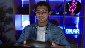 A focused man wearing headphones sits in a neon-lit gaming room at night, portraying modern entertainment.