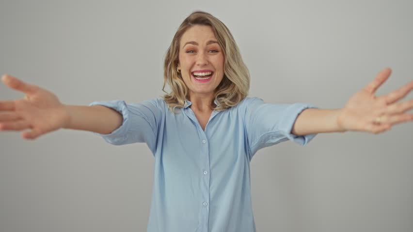 Joyful young blonde woman fashioning a shirt, arms wide open offering a hug! smiling at the camera, full of happiness on a white isolated background. Royalty-Free Stock Footage #3487113453
