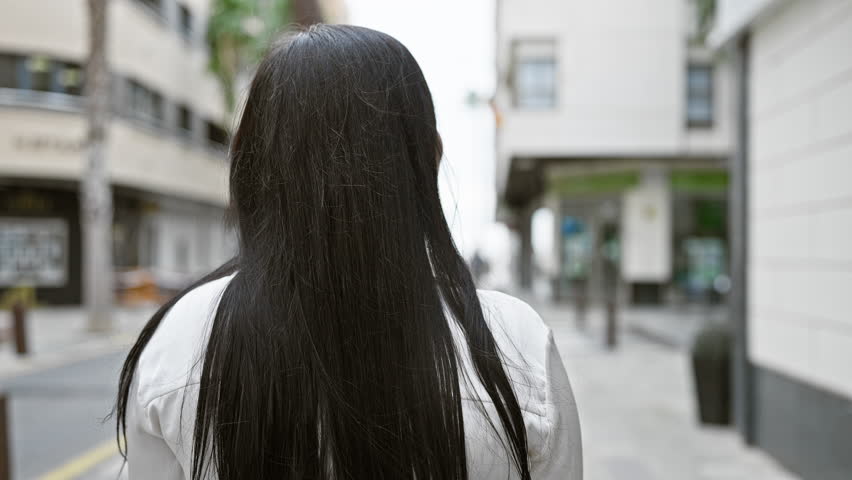 A young hispanic woman walks on an urban street, exuding confidence and style in the city.