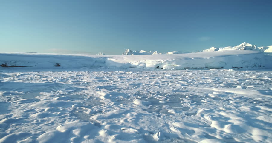 Aerial fly over snow covered hill landscape in Antarctica. Towering mountains in the background under clear blue sky. Antarctic majestic winter landscape drone view. Discover the beauty of South Pole