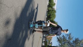 Vertical video of a father carrying his little son on a scooter. Happy family outdoors. High-quality shooting in 4K format. The concept of rest, coordination of movements, balance, attention, skill