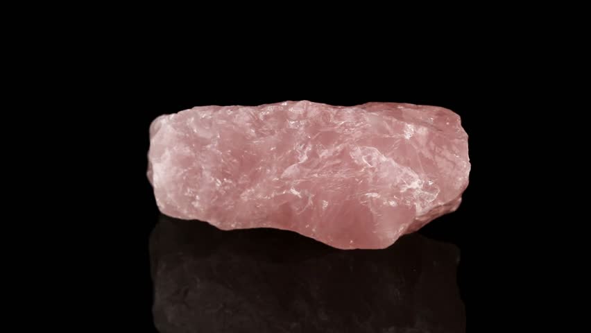 Polished mineral stone rose quartz rotates in a circle on a black background close up