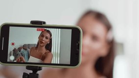 Young social medial content creator woman make fashion video. Blogger smiles to camera using selfie stick and light ring while making persuasive online clothing sell vlog to audience or follower. Adit