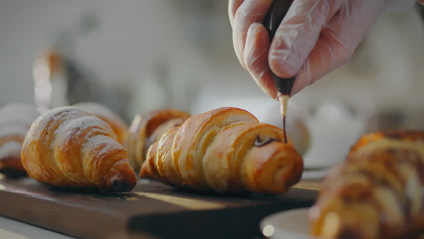 Dough. Master pastry chef pours fresh chocolate over a croissant in a production kitchen. An experienced man pours dark chocolate over baked goods and masters new recipes for baking, assorted