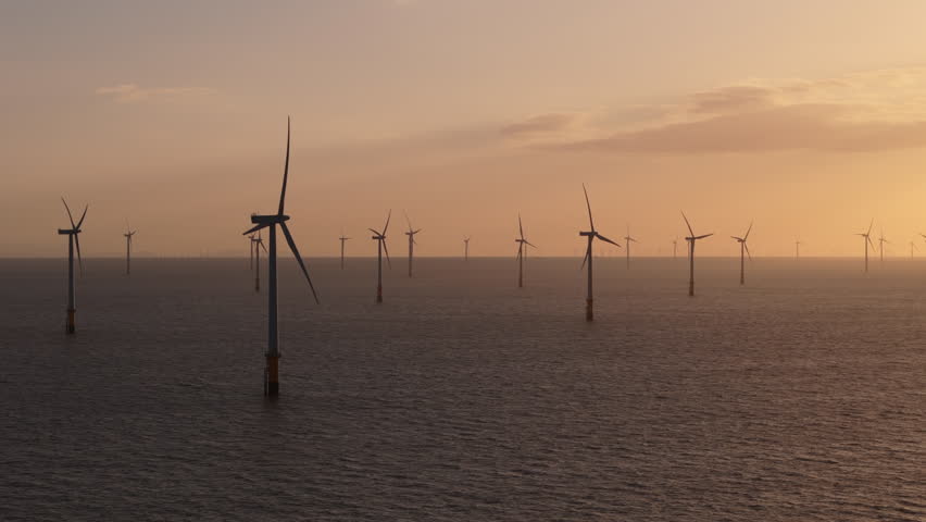 Beautiful view of offshore wind turbines spinning at sunset with dramatic sky and clouds in background