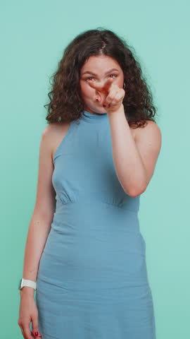 I am watching you. Young confident woman pointing at her eyes and camera, show I am watching you gesture, spying on someone. Attractive brunette girl isolated alone on blue studio background. Vertical