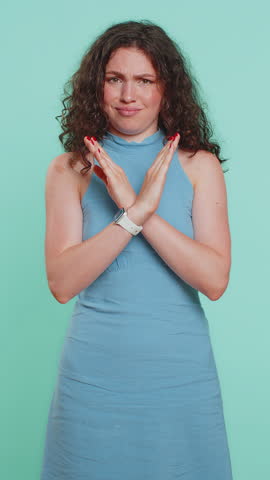 Young woman say No hold palm folded crossed hands in stop gesture, warning of finish, prohibited access, declining communication, body language, danger. Girl on blue background. Lifestyles. Vertical