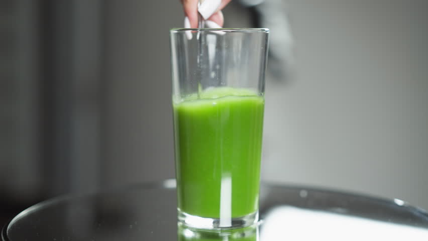 Index finger gently pressing on surface of fresh green vegetable juice in a clear glass