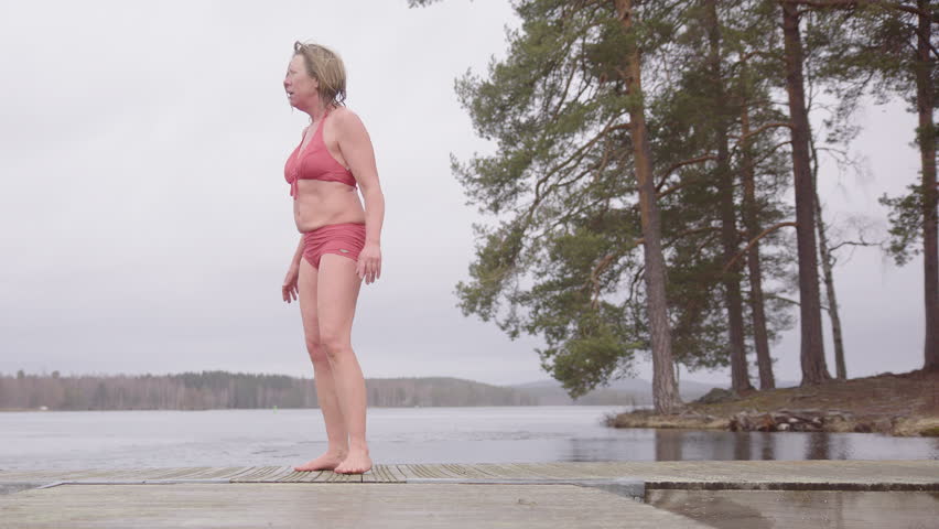 Emotional woman in togs warms up with Wim Hof method on pontoon after ice bath