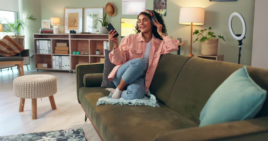 Home, karaoke and girl listening to music with headphones, phone and streaming audio online. Kpop, sound and happy woman relax on sofa with smartphone, app and hearing playlist with excited energy Royalty-Free Stock Footage #3487362083