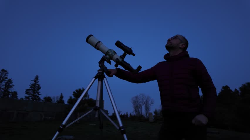 Amateur astronomer looking at the evening skies, observing planets, stars, Moon and other celestial objects with a telescope.