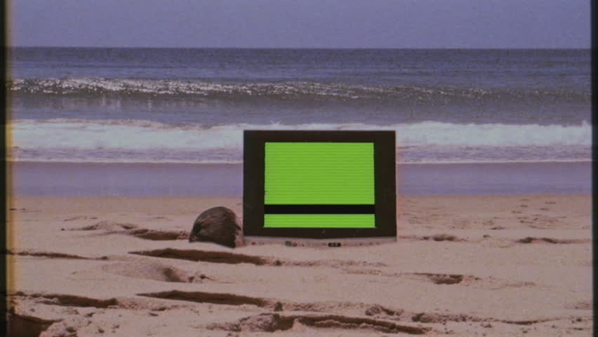 Old TV Green Screen Beach Shore Vintage Television VHS Effect Zoom In. Vintage television with green screen laying on the sand of a beach on a sunny day, VHS texture. Zoom In