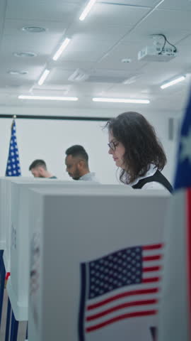 Vertical shot of multiethnic American voters voting in booths in polling station office. National Election Day in the United States. Political races of US presidential candidates. Concept of civic