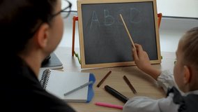 Preschool teacher teaching child alphabet. Preschool girl learning alphabet letters, using chalkboard. Individual Primary Education