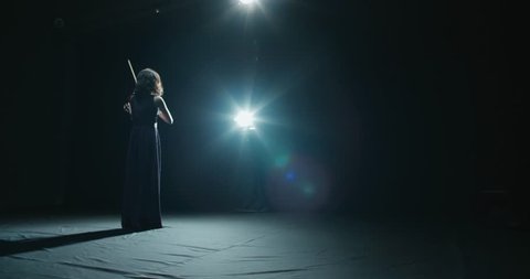a talented girl violinist performs at her first solo concert, stage light, dark background
