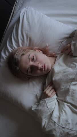 Depressed young woman lying on bed, female insomnia at night. Vertical video.