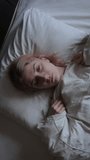 Depressed young woman lying on bed, female insomnia at night. Vertical video.