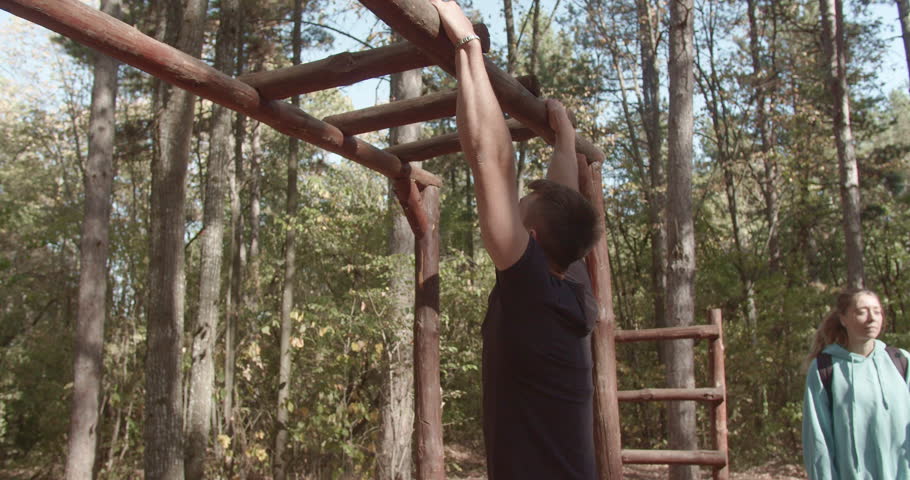 Surrounded by woods, a fit young male exercises using a pull-up bar outdoors, showcasing strength and a commitment to a healthy lifestyle amidst the beauty of nature. Royalty-Free Stock Footage #3487741679