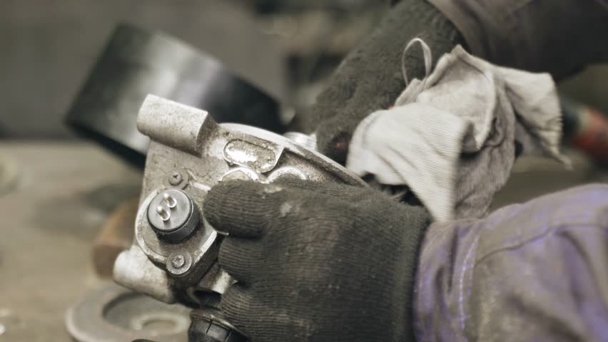 A mechanics hands in gloves meticulously cleaning and inspecting a car part on a workbench in a workshop.