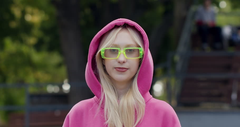 Smiling girl wearing chameleon glasses takes off hood closeup. Female teenager shows Victory sign with fingers during photo shot. Active lifestyle