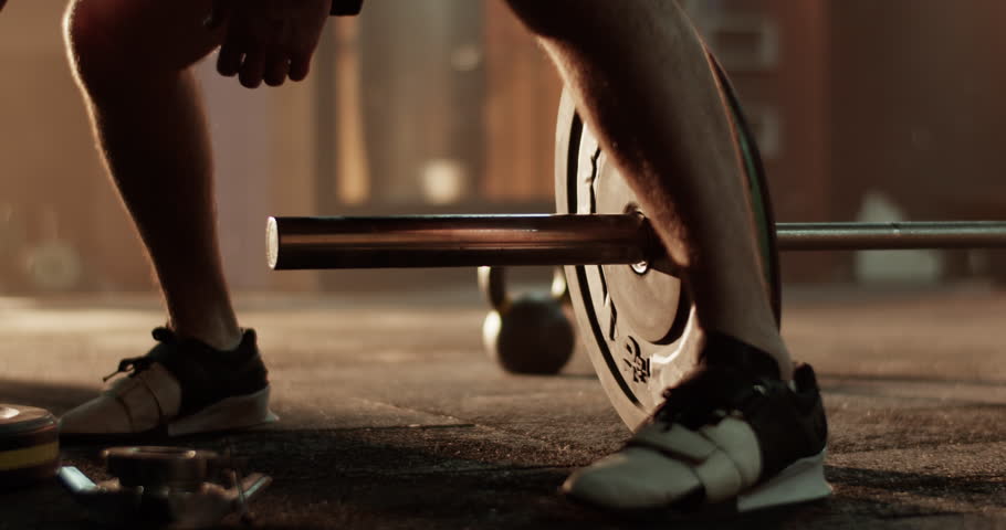 Unrecognizable man athlete adding weight plate on barbell