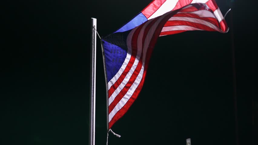 Close up slow motion 120fps the National Flag of the United States of America waving in the wind at night illuminated by street lamp. Symbol of Democracy and independence 