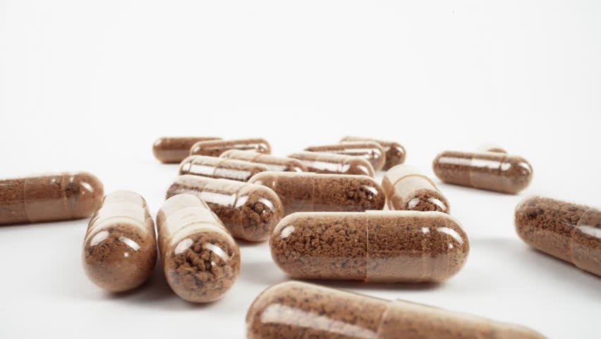 Close-up of two herbal capsules in sharp focus against a bright white background