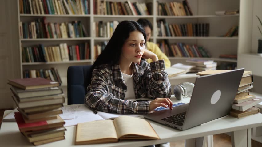 Charming confident girl preparing for exam at university studying and typing at library workplace Pretty student looking at laptop computer screen indoors Distance remote education
