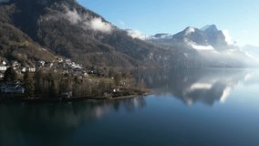 Panning drone clip of picturesque Swiss town on edge of calm lake, on bright spring day with blue skies