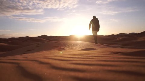 A lonely man walking into a desert in slow motion.