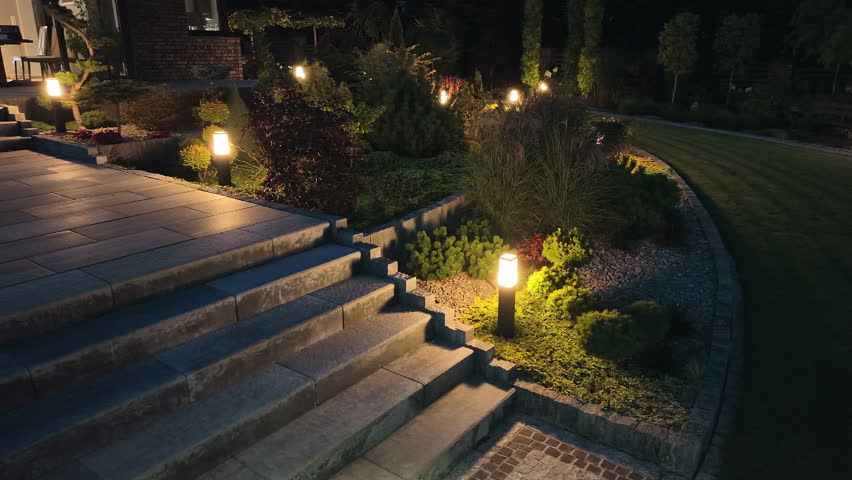 Beautiful Backyard Garden Illuminated with Outdoor Lamps in the Evening. Professional Gardening Theme.