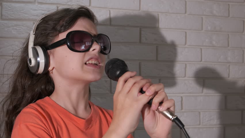Child active leisure with karaoke microphone. A joyful little girl pass her free time with microphone in the room. A concept of joyful time during childhood.
