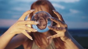 Portrait of a beautiful red-haired girl engaged in contact juggling with an acrylic ball, which remains motionless as she holds it between the tips of her dexterous fingers. Close up. Slow motion. 4k - Powered by Shutterstock - Get 15% off with code: PIKWIZARD15