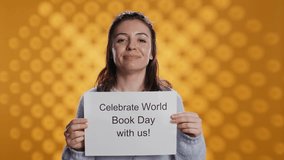 Portrait of happy woman holding placard with world book day message written on it, isolated over studio background. Geek promoting importance of reading during 23th April global event, camera B