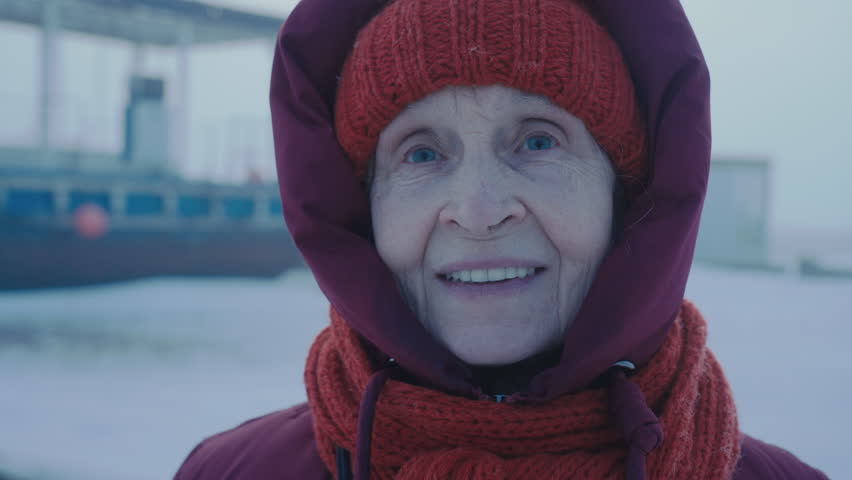 A happy woman looks at the camera and blinks. Aged female tourist traveling North Pole. Petrol station in the Arctic. Oil and gas industry base worker. Extreme cold. Petroleum technician. 