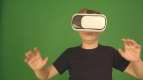 Boy in VR glasses. closeup shot. The boy looks emotionally virtual glasses. Child in a green background. Camera in 4K.