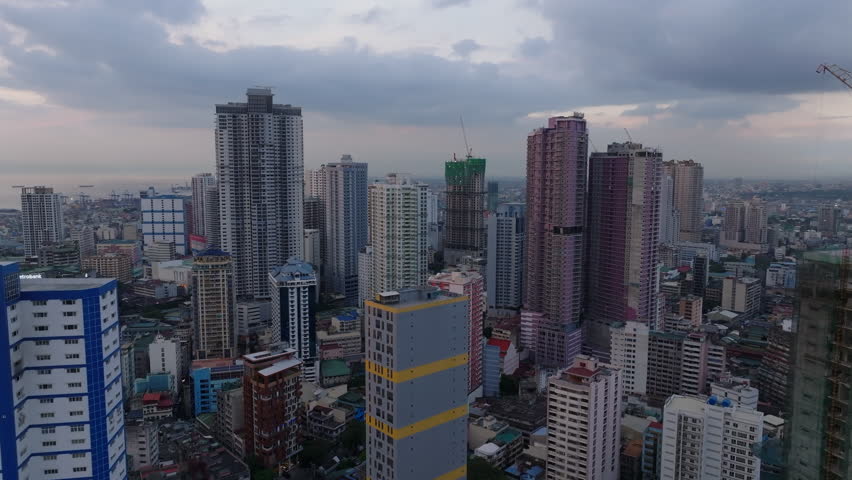 Aerial ascending footage of modern high rise residential buildings in urban borough. Panoramic view of metropolis at twilight. Manila, Philippines