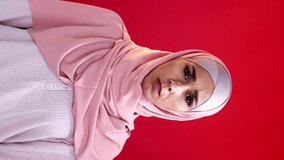 Vertical video. Omg shock. Regret sorrow. Grief compassion. Overwhelmed sad upset woman in hijab covering mouth with hands isolated on red copy space background.