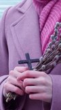 Close-up of female hands holding a small bouquet of willow branches and a wooden Orthodox cross. Palm Sunday, Easter. Religion, hope, faith. Vertical video, shorts.