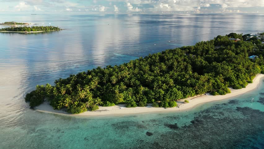 Aerial drone video slowly flying around the local island of Thinadhoo at sunrise in the Maldives.