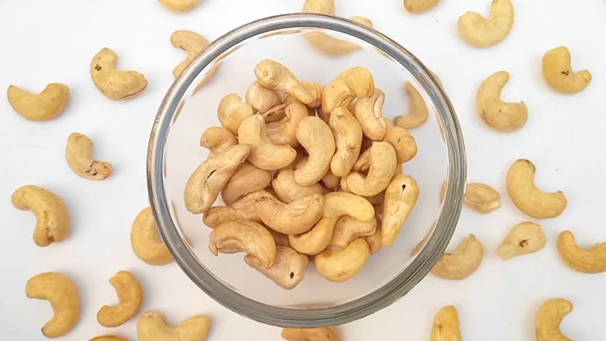 Cashew nuts without shell in a glass bowl on white background from overhead. rotates, close up. Dried cashew nuts. Raw snack.