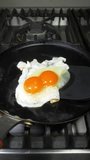 Vertical video - Closeup of a large double yolk hen’s egg, being turned over with a spatula as it fries in a steaming hot pan, on a kitchen stove.