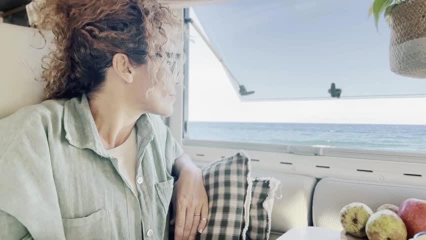Curly woman looks at her laptop monitor which she uses to communicate with friends and family online. Attractive woman traveling, staying overnight in her camper van at an RV camping area