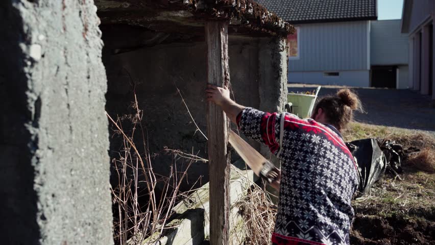 The Man is Using a Saw to Cut Through the Aged Support Post Located on the Farm in Indre Fosen, Trondelag County, Norway - Static Shot