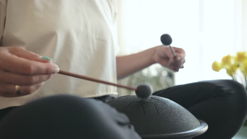 Relaxed curly brunette sitting in lotus pose on the kitchen table and playing tank drum