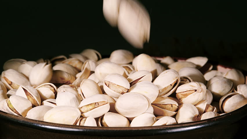 Dried Pistachio Nuts with Cracked Shells and Green Kernels Falling into a Rustic Ceramic Bowl Closeup in Slow Motion