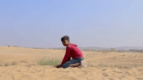 boy playing with yellow sand at desert at day video is taken at rajasthan, India.